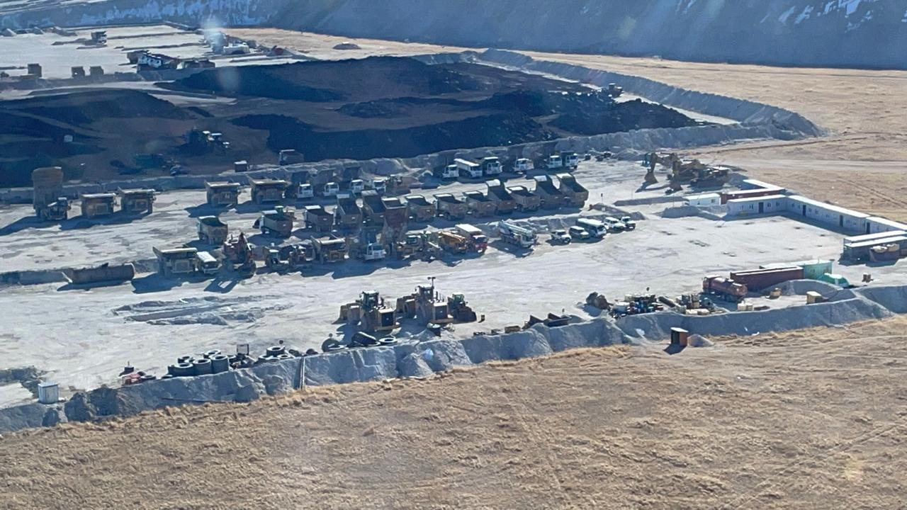 Haul trucks and loaders drawn up on a mine bench beside an exposed coal seam
