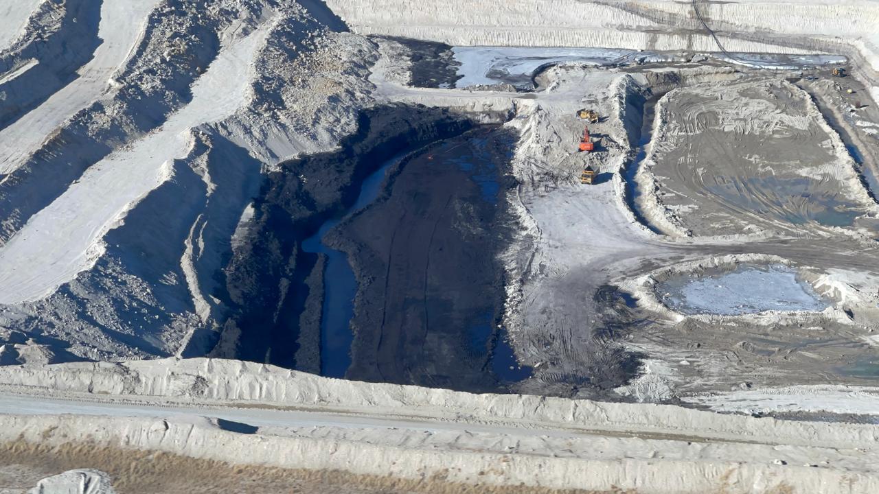 Close aerial of the working face, with standing water and excavators on the pit floor